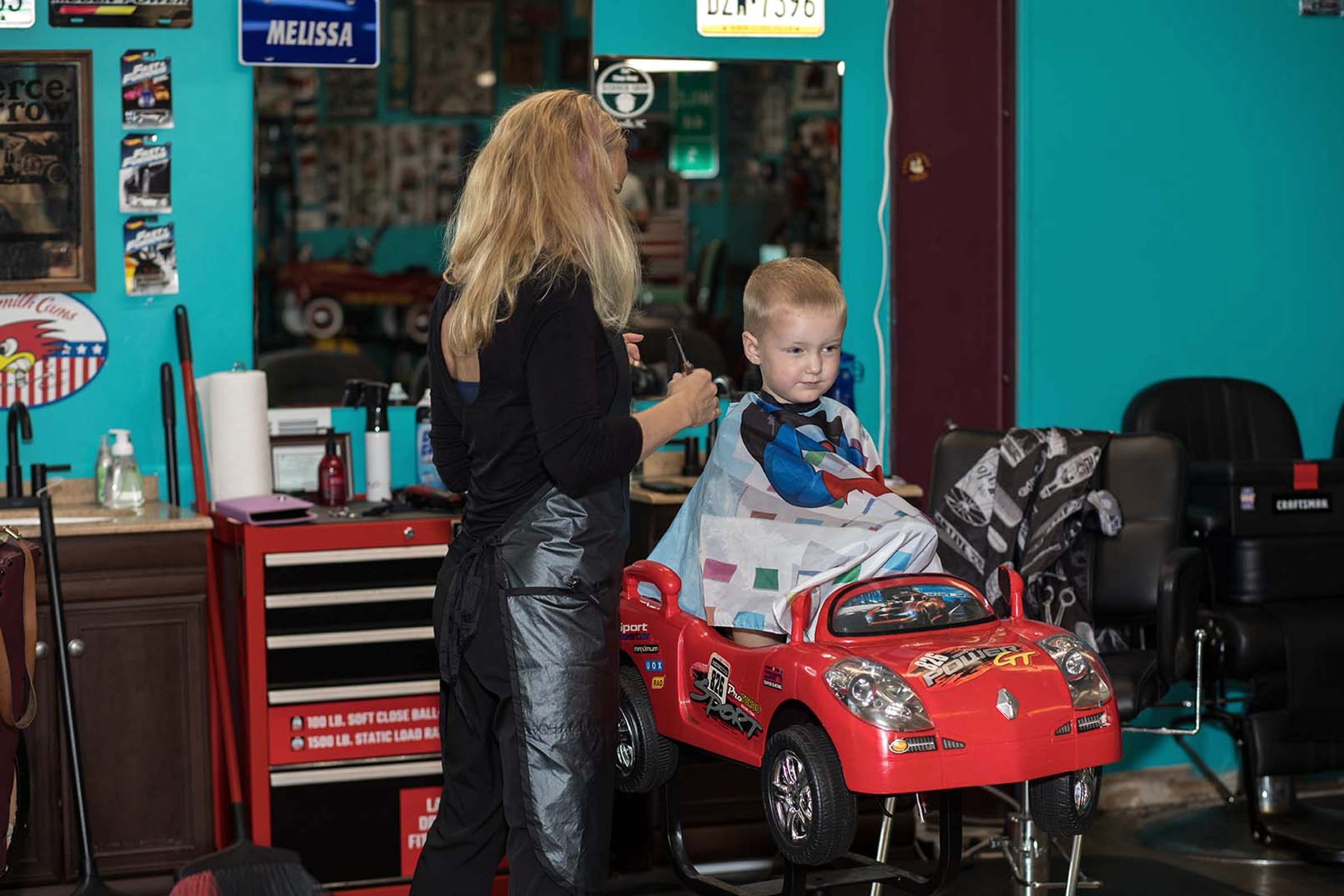 A barber giving a young child a haircut in The Chop Shop car chair